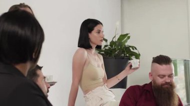 Değişik bir ekip, sıradan bir ofis ortamında bir daire içinde oturup bir iş toplantısına katılıyor. Kahve ve suyun tadını çıkarırken iş tartışıyorlar..