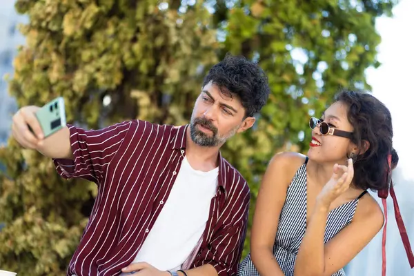 Neşeli bir çift güneşli bir günü dışarıda geçirirken selfie çekiyor. Yeşilliklerle çevrili boş zamanlarının tadını çıkarıyorlar..