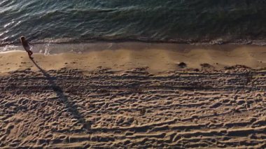 Genç bir kadın gün doğumunda ya da gün batımında sahilde yürür. Hava görüntüsü. Rahatlama, tatil, yaşam tarzı kavramı..