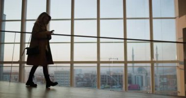 Priştine ve Kosova 'ya bakan geniş pencereli çağdaş bir binada genç bir kadın yürüyor ve konuşuyor.