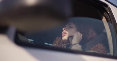 Dişlerinde diş teli olan neşeli genç bir kadın akıllı telefonunu arabada kullanıyor, mutluluk ve bağlantı yayıyor..