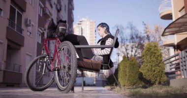 Açık havada oturan genç bir kadın akıllı telefonuyla selfie çekiyor. Çağdaş kentsel bir mahallede arkasında park etmiş bir bisiklet..