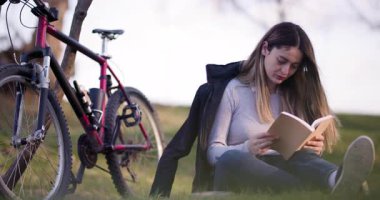 Gün batımında yakalanan bu resimde, dağ bisikletlerinin yanında huzur içinde kitap okuyan genç bir kadın açık havada huzurlu bir anın tadını çıkarıyor..