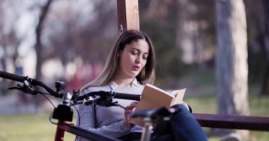 Huzurlu bir parkta yakalanan bu resim, yanında bisikletiyle kitap okuyan, dışarıda huzurlu bir anın tadını çıkaran genç bir kadını gösteriyor..