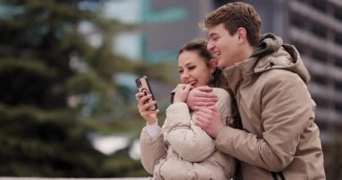 Genç bir adam ve bir kadın kentteki akıllı bir telefona bakıp samimi bir neşe ve bağlantı anını yakalarken birlikte gülüyorlar..