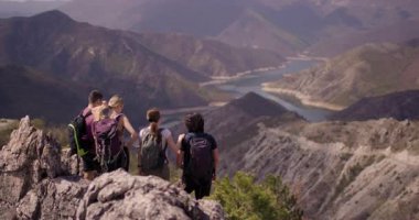 Dört arkadaştan oluşan bir grup, engebeli arazinin ortasındaki dolambaçlı bir nehri gören bir dağın zirvesinde zafer için kollarını kaldırdılar. Sırt çantalarıyla donatılmışlardır. Neşe ve özgürlüğü yakalarlar.