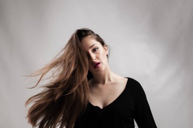 Siyah elbise giyen genç bir kadının zarif ve dinamik stüdyo portresi, uzun saçları gri bir zemine çarpıcı bir şekilde akıyordu..