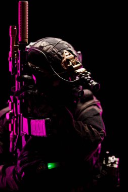 Ağır silahlı bir özel kuvvetler ajanının dramatik ışıklandırmayla aydınlatılmış bir görüntüsü. Askeri hazırlık, strateji ve ileri teknoloji temalarını kavramsallaştırır.