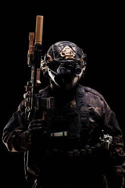 Tüfek ve gece görüş gözlüğü ile donatılmış ileri savaş teçhizatı giymiş askeri bir şahıs, güvenlik, taktik uzmanlık ve düşük ışık koşullarında anonimliği vurguluyor.