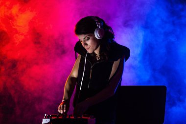 Karıştırıcıda müzik çalan kadın DJ. Kırmızı ve mavi ışıklar ve arka planda duman