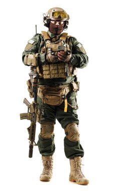 Tam teçhizatlı ve miğferli bir asker, elinde tüfekle gezici bir cihaz kullanır. Askeri operasyonlarda modern askeri teçhizat, hazırlık ve teknolojik iletişimi gösteriyor.