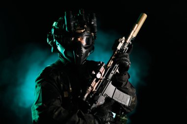 İleri düzey taktik teçhizat takan ve elinde tüfek tutan bir asker, esrarengiz yeşil ışıklı bir geçmişe karşı, hazır olmayı, stratejiyi ve yüksek teknoloji askeri teçhizatı sembolize ediyor..