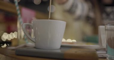 Sıcak bir kafede sıcak çikolata karıştıran bir elin yakın çekimi, sıcak bokeh ışıklarıyla çevrili, sıcak ve rahat bir anı yakalıyor..