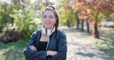 Parkta şık bir genç bayan. Kulaklıklı güzel kız kameraya bakıyor. Sol kamera hareketi.