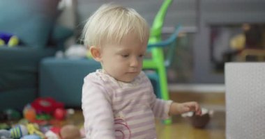 Sarışın, tatlı bir çocuk, oturma odasında yere saçılmış renkli oyuncaklarla oyun oynamaktan zevk alıyor. Onun masum merakı ve dikkati çocukluk çağındaki gelişimin mucizesini vurguluyor..