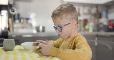 Genç bir çocuk yemek yerken mutfak masasında cep telefonuna daldı..