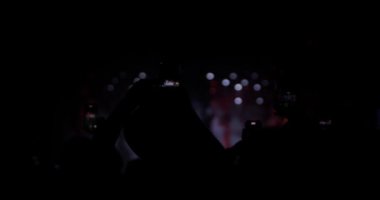 Kalabalığın içindeki soyut siluet insanlar ellerini kaldırıp dans ediyorlar ve ellerinde akıllı telefonlar tutuyorlar. Işık yanıp sönüyor ve odak noktasını kaybediyor