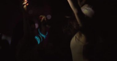 Sahnenin önünde dans eden iki genç kız. Zıplıyor ve öpücük yolluyor. Arka planda odak dışı insan kalabalığı.