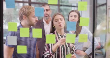 İş arkadaşları proje projelerini tartışıyor. Kafkas iş adamlarından oluşan bir ekip cam pencerenin yanında yapışkan notlarla bekliyor. Renkli çıkartmalı Scrum metodolojisi. 