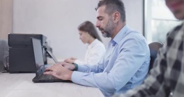 Ofisteki insanlar dizüstü bilgisayarlar ve bilgisayarlar üzerinde çalışıyorlar. İş arkadaşları takımı. Saha videosunun derinliği. Geriye dönük kamera hareketi.