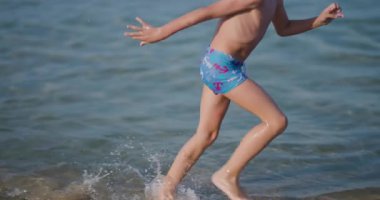 Sahilde oynayan enerjik çocuklar güneşli bir günde kıyı şeridi boyunca koşuyorlar. Yaz eğlencesinin, özgürlüğün ve açık hava macerasının mükemmel tasviri..