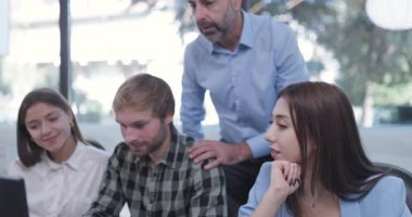 Ofiste çalışan genç iş arkadaşları. Kıdemli amir ayakta duruyor ve tavsiye veriyor. Başarılı ekip bir sorunu çözüyor.