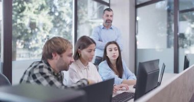 Ofiste çalışan genç iş arkadaşları. Kıdemli amir ayakta duruyor ve tavsiye veriyor. Başarılı ekip bir sorunu çözüyor.