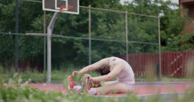 Kendini adamış bir bayan sporcu, bir basketbol topuyla, odaklanmış ve dengeli bir şekilde, açık bir sahada, zihinsel ve fiziksel olarak bir maça hazırlanıyor..
