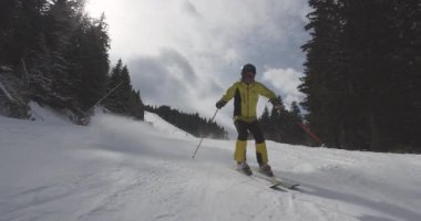 Parlak sarı dişli bir kayakçı, karlı bir yamaçta ustalıkla yol alır, çarpıcı dağ manzarasının ortasında kış sporlarının heyecanının tadını çıkarır..