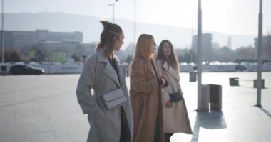 Arkadaşlar şehirde güneşli bir günün tadını çıkarıyorlar, dışarıda sohbet ediyorlar ve birlikte yürüyorlar..