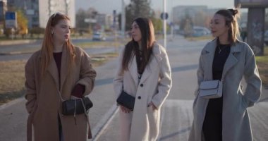 Üç modaya uygun kadın güneşli bir günün tadını çıkarıyorlar, şehirde geziniyorlar ve sohbet ediyorlar, şehir atmosferini sergiliyorlar..