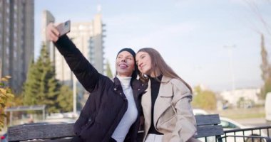 İki arkadaş şehirde güneşli bir günün tadını çıkarıyorlar, selfie çekiyorlar ve birlikte gülüyorlar..