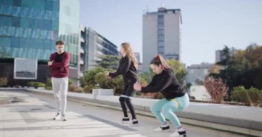 İki zinde genç kadın direniş bantları kullanarak çömelme hareketleri yapıyor, antrenörlerinin teşviğiyle fitness ve takım çalışması sergiliyorlar..