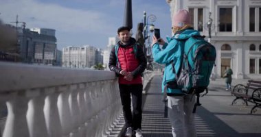 Sırt çantalı genç bir adam ve kadın bir şehri keşfediyor, fotoğraf çekiyor ve telefonlarını navigasyon için kullanıyor..