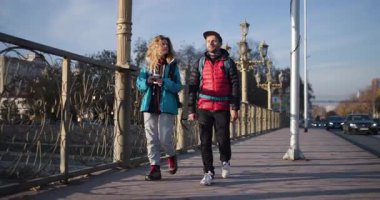 Parlak ve güneşli bir sonbahar gününde, şehir köprüsünde sakin bir gezinti sırasında, çiftler yürüyüp sohbet eder, kahvenin tadını çıkarırlar..