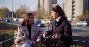 İki bayan arkadaş ya da iş arkadaşı tabletteki bir şeyi tartışıyor. Şehir, sonbahar, bankta oturmak. İş Kadınları.