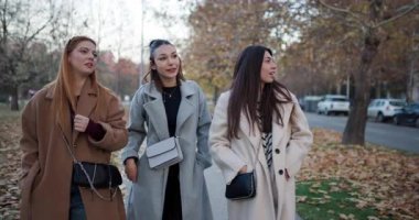 Arkadaşlar sonbaharda parkta birlikte yürür, eğlenceli bir sohbet eder ve gülerler..