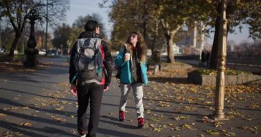 Sırt çantalı genç bir adam ve kadın sonbaharda parkın içinde yürürler, manzaranın tadını çıkarırlar ve birbirlerine eşlik ederler..