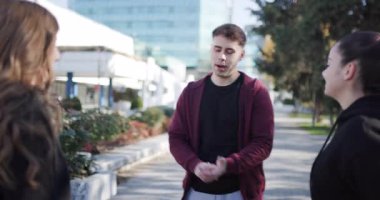 Bir grup genç yetişkin şehir parkı ortamında eğleniyor, sohbet ediyor ve gülüyor..