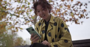 Heyecanlı genç bayan, sonbahar boyunca parkta bir bankta otururken telefonundan iyi haberler alıyor..