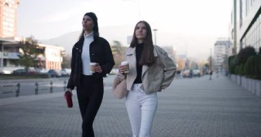 İki bayan arkadaş sabah gezintisinin tadını çıkarıyorlar. Yürürken kahve içip sohbet ediyorlar..