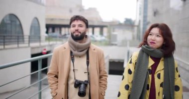 Genç bir adam ve kadın şehirde birlikte yürüyüp konuşurlar. Şık kışlık kıyafetler giyip mutlu ve nişanlı görünüyorlar..