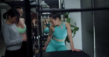 Modern bir spor salonunda üç kadın güçlü bir antrenman yapıyor. Antrenman teknikleri üzerinde işbirliği yapıyorlar ve birbirlerini daha iyi performans için motive ediyorlar..