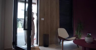 Hafif giyinmiş bir kadın zarif bir şekilde çağdaş bir binaya girer. İç kısımda parlak tasarım elementleri ve geniş pencereler var, doğal ışığın içeri akmasına olanak sağlıyor..