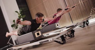 İki adam şık bir fitness stüdyosunda yenilikçi bir pilates çalışması yapıyor. Özel ekipmanları kullanırken güç eğitimi ve denge üzerine odaklanırlar..