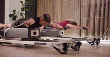 İki adam doğal ışıkla dolu şık bir fitness stüdyosunda yenilikçi pilates egzersizleri yapıyor. İşbirlikçi bir ortamda güç ve esneklik oluşturmaya odaklanırlar..