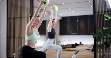 Çağdaş bir spor salonunda enerji antrenmanına katılan iki kadın, güçlerini ve koordinasyonlarını arttırmak için yeşil egzersiz toplarını kullanıyorlar..
