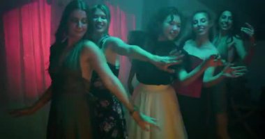 Arkadaşlar loş ışıklı bir odada renkli ışıklar altında dans ederler. Gülümsüyorlar ve birbirlerine eşlik etmekten zevk alıyorlar..
