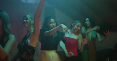 Bir ev partisinde dans eden arkadaşlar. Renkli ışıklar odayı aydınlatıyor. Müzikten zevk alıyorlar ve kutluyorlar..