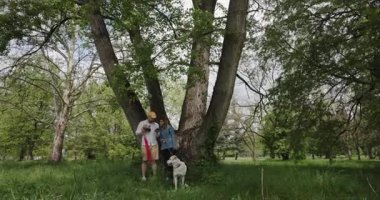 Bir çift köpekleriyle birlikte büyük bir ağacın gölgesinin altındaki parkta selfie çekiyor. Birlikte dışarıda vakit geçirmenin tadını çıkarıyorlar..